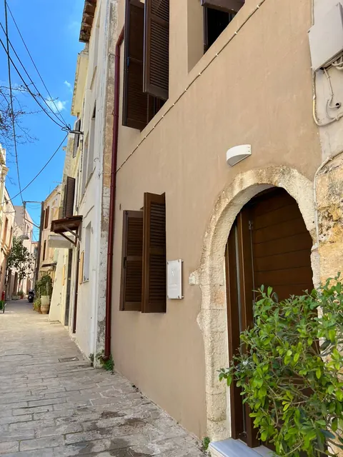 Facciata sul vicolo lastricato, con porta ad arco in pietra e persiane in legno